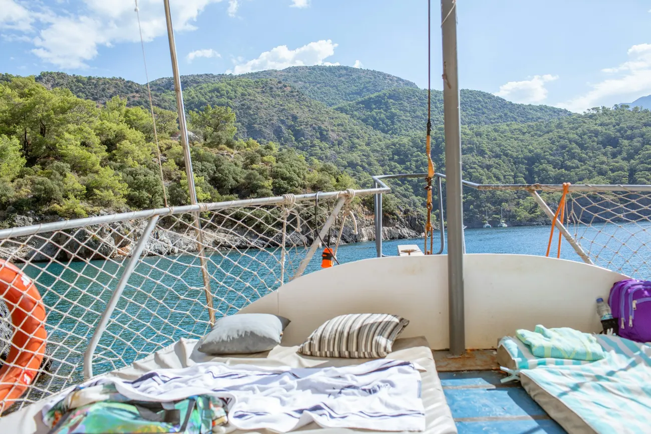 Sonniges Bootsdeck mit Kissen, dahinter eine bewaldete Küste